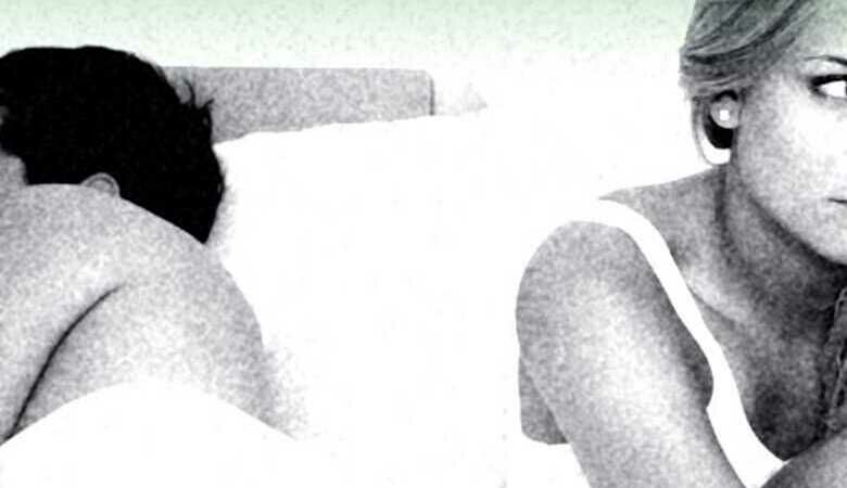 Mann und Frau liegen Rücken an Rücken in einem Bett, die Frau schaut gefrustet