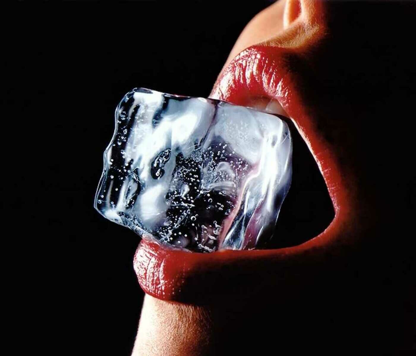 Großaufnahme eines weiblichen, rot geschminkten, Munds mit einem Eiswürfel zwischen den Lippen