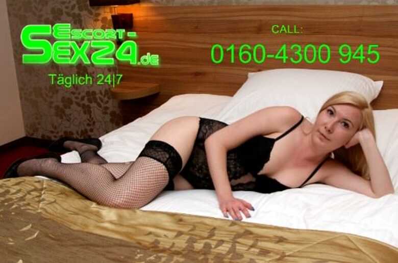 Escortmodel Anette liegt in schwarzer Unterwäsche und High Heels auf einem Bett